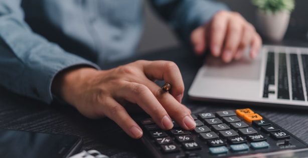 Person using a calculator and laptop for bookkeeping or financial work.